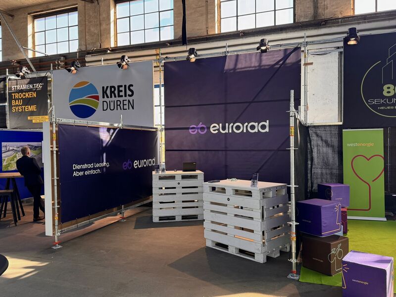 Trade show booth for Eurorad featuring company banners, white wooden pallet table, boxes, and signs for Kreis Düren and Westenergie at a business or technology expo